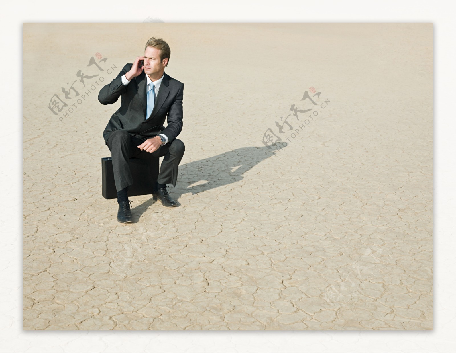 干旱地里坐着皮箱打手机的商务男士图片