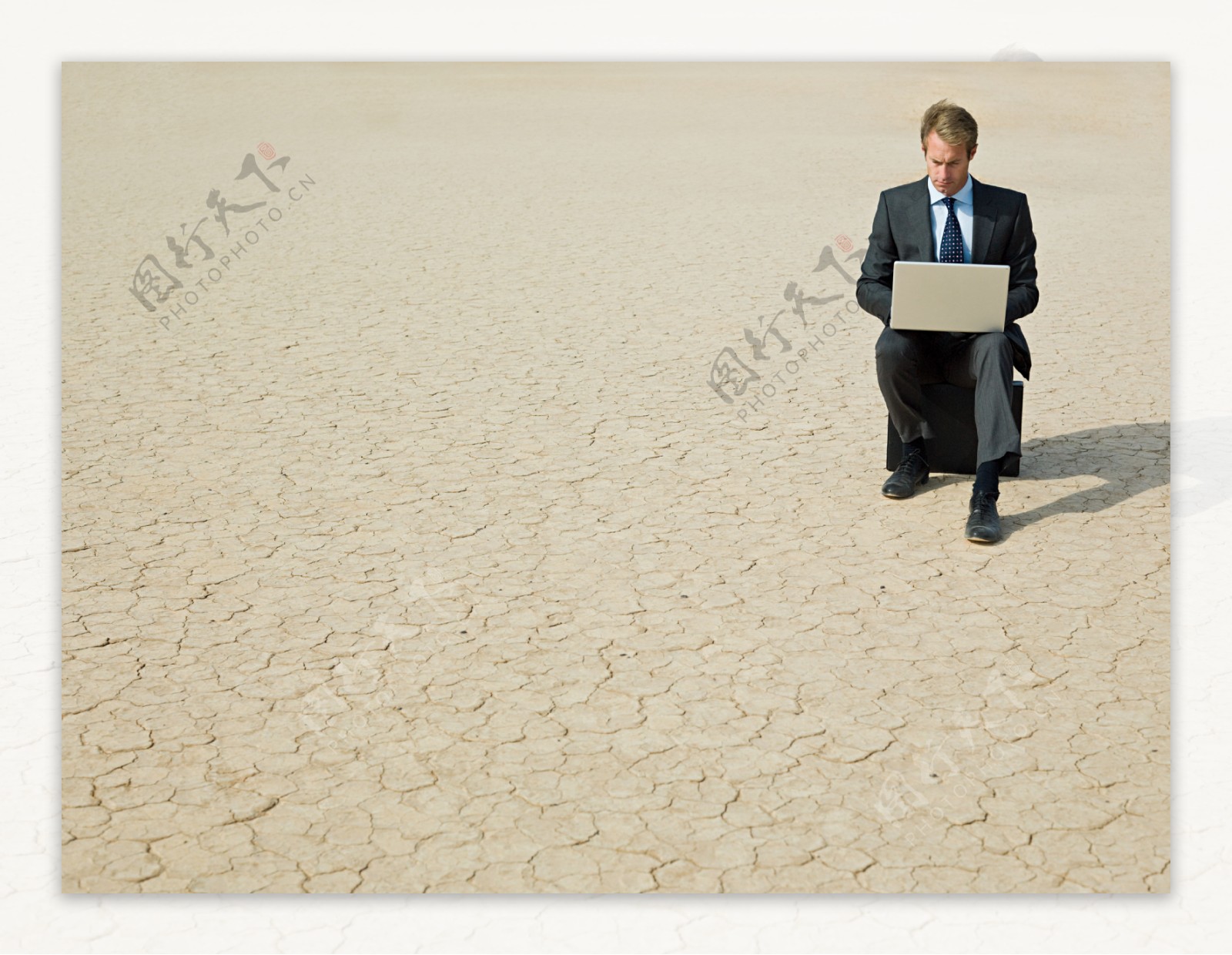 在干旱土地里打电脑的商务男士图片